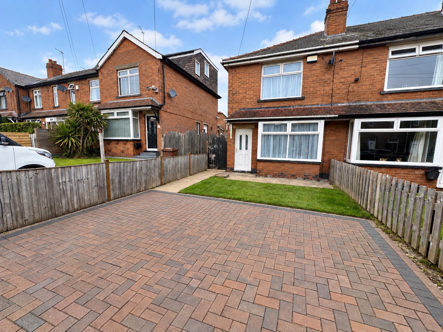 Brick semi-detached house with driveway, garden, wooden fencing and clear sky