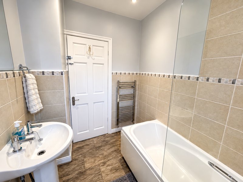 Modern bathroom with pedestal sink, bathtub, glass shower screen and heated towel rail