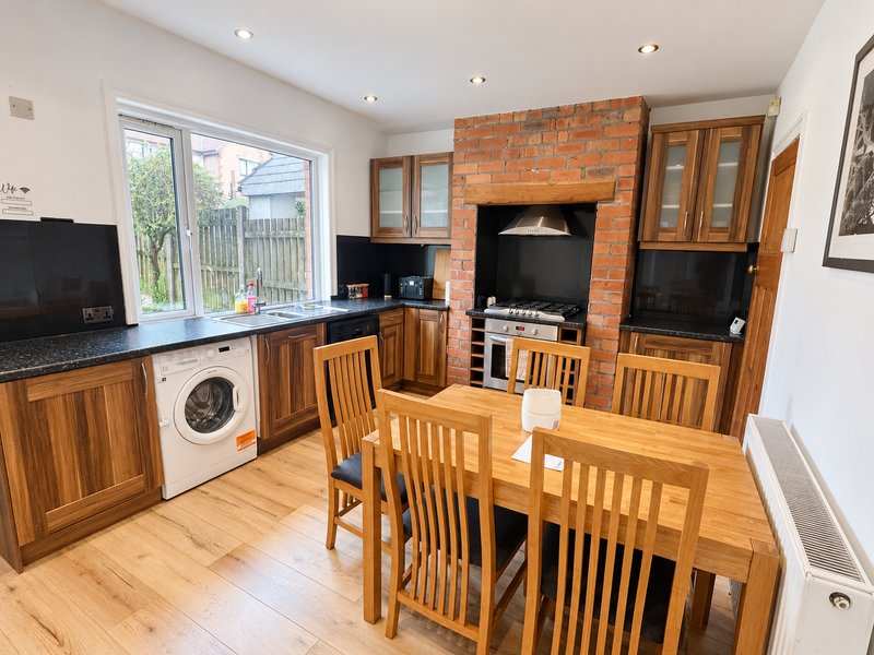 Open-plan kitchen-diner with wooden cabinets, dining table, washing machine and brick fireplace