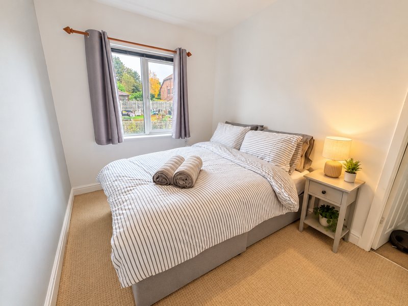 Bright modern bedroom with double bed, striped bedding, wooden nightstand and window view