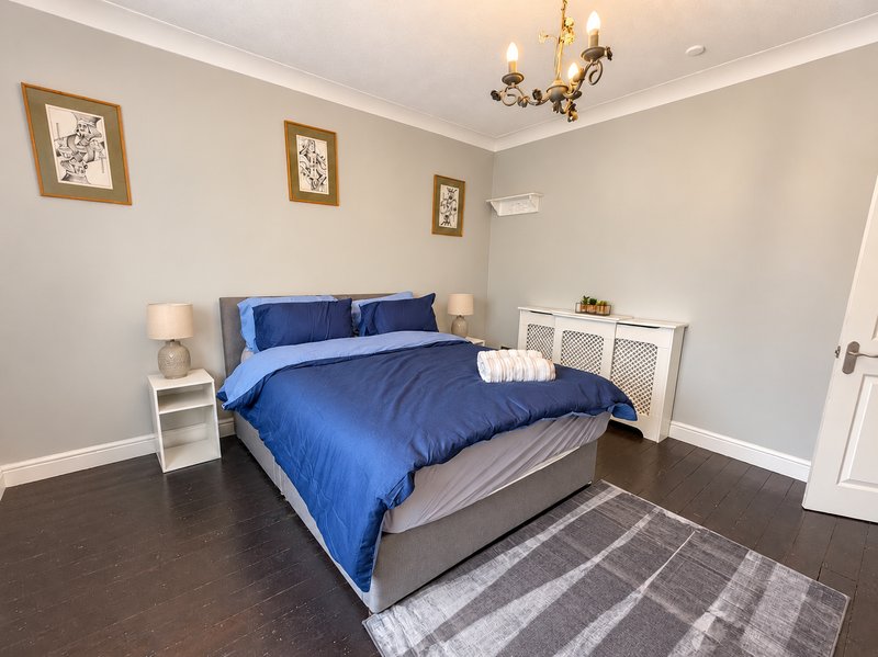 Spacious bedroom with blue bedding, white storage furniture, dark wood flooring and framed wall art