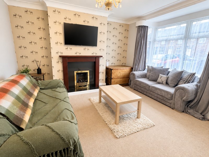 Bright living room with fireplace, wall-mounted TV, two sofas and large windows with curtains