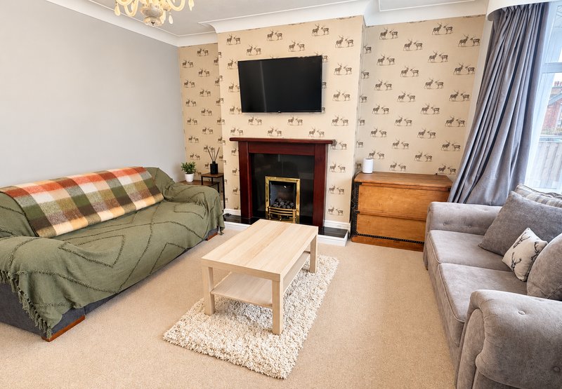 Spacious living room with fireplace, sofas, TV, patterned wallpaper and wooden furniture