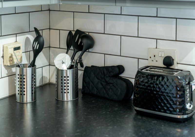 Kitchen countertop with utensil holders, black appliances, and white subway tile backsplash