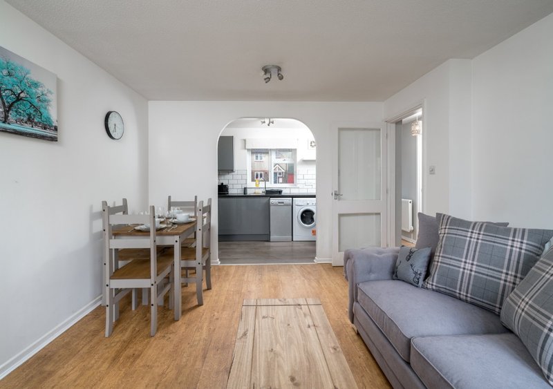 Open-plan living area with wooden dining table, sofa, and kitchen visible through archway