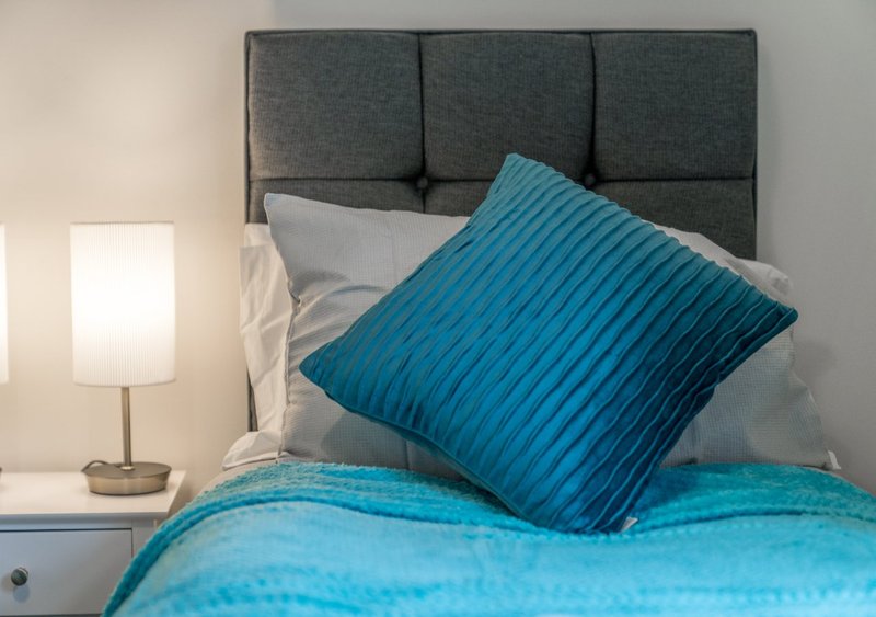 Bedroom with gray upholstered headboard, turquoise bedding, pillows, and table lamp