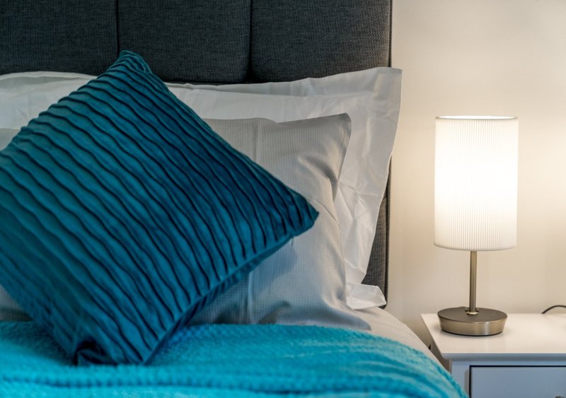 Bedroom with teal striped cushion, white pillows, grey headboard and table lamp