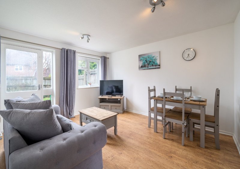 Open-plan living and dining area with grey sofa, wooden dining table, TV, and patio doors