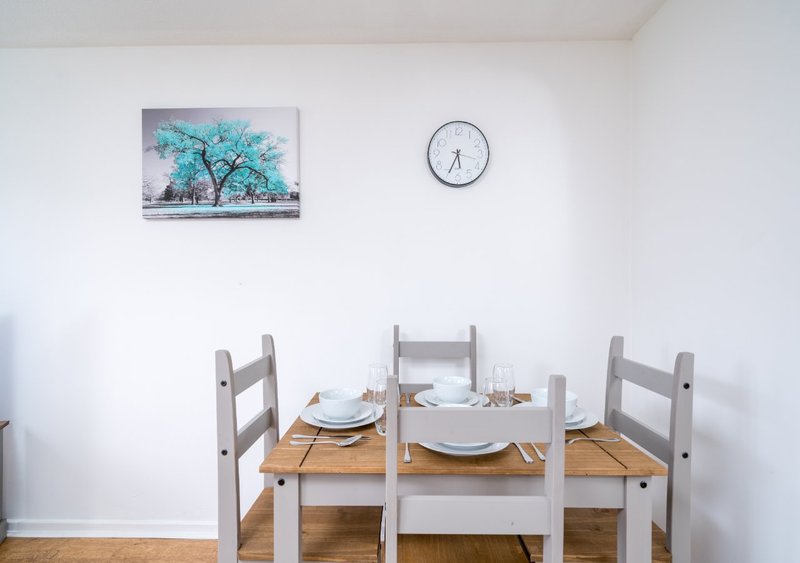 Dining area with wooden table, grey chairs, place settings and wall clock