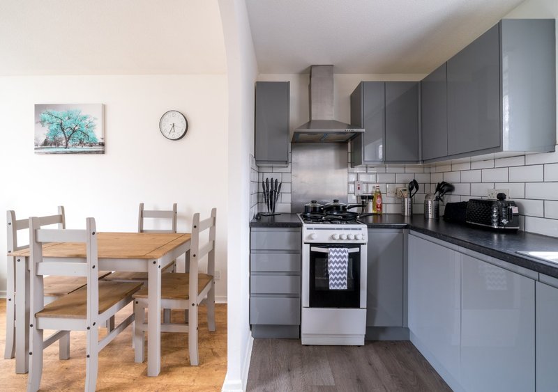 Open-plan kitchen and dining area with grey cabinetry, white cooker, and wooden dining table with chairs