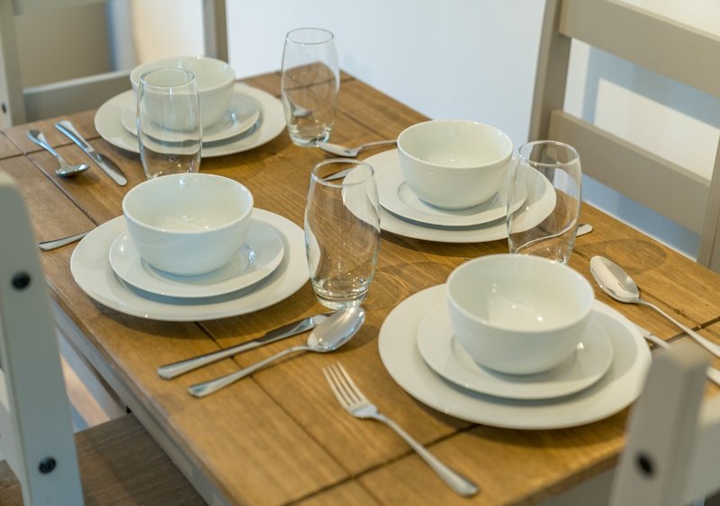 Dining table set for four with white dishware, glasses, and cutlery