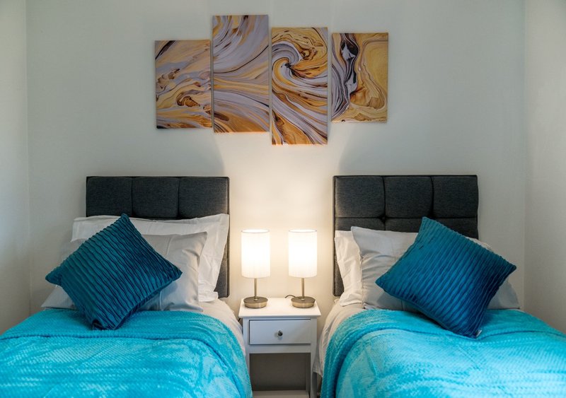 Twin bedroom with turquoise bedding, black headboards, blue cushions and abstract wall art