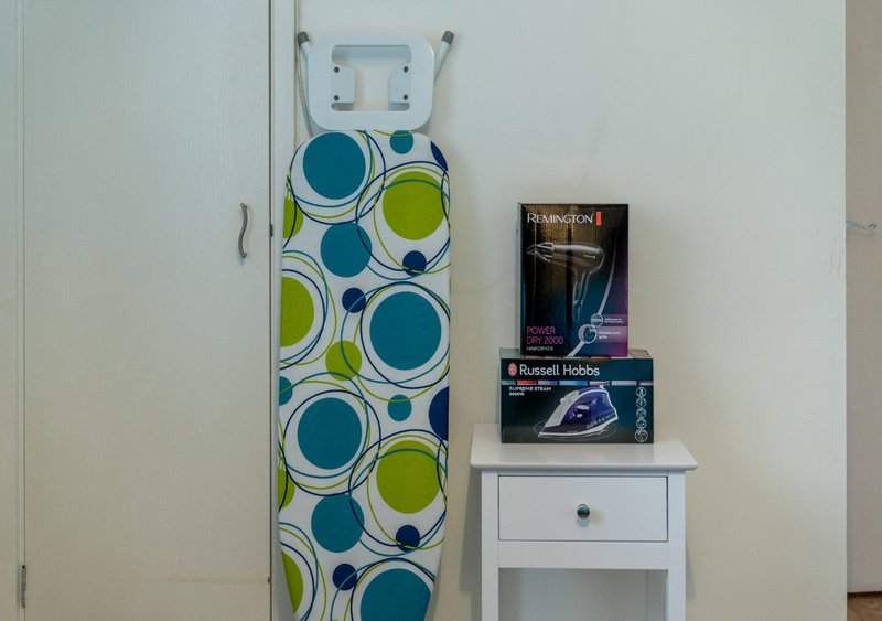 Laundry area with ironing board, iron, and small white side table with appliance boxes