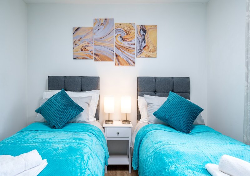Twin bedroom with turquoise bedding, grey headboards, and abstract wall art