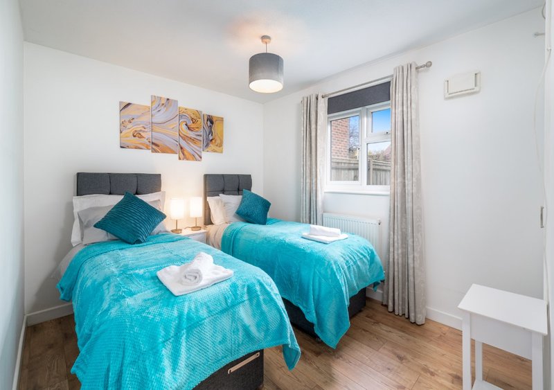 Twin bedroom with turquoise bedding, teal cushions, wooden floor and window