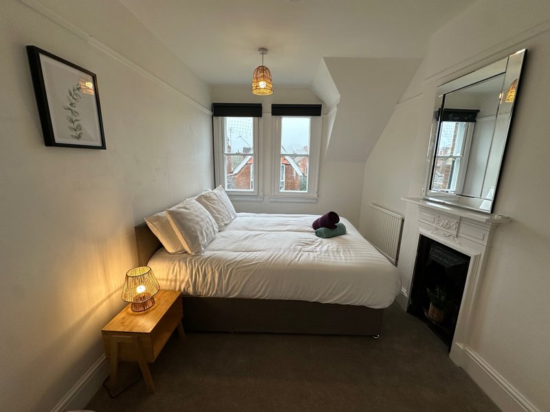 Bright bedroom with single bed, wooden nightstand, mirror, framed wall art and French doors