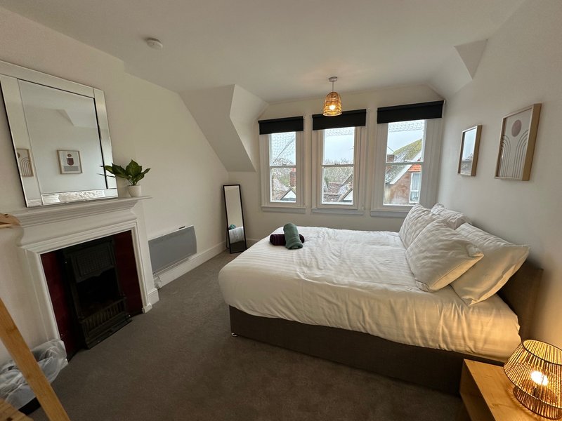 Bright bedroom with double bed, fireplace, mirror, and large windows overlooking trees