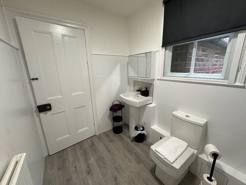 Clean bathroom with white wall-mounted sink, toilet, window, and laminate flooring