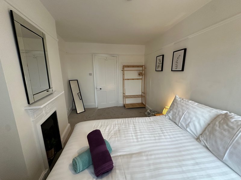 Bright bedroom with double bed, white walls, fireplace, and wooden shelving unit