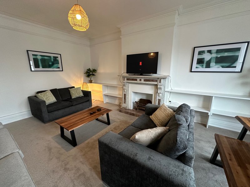 Spacious living room with two grey sofas, wooden coffee table, fireplace, TV, and framed wall art