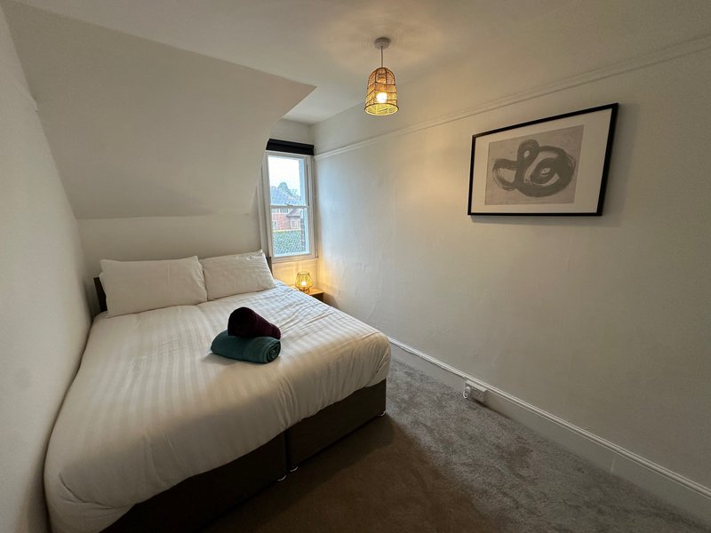 Compact bedroom with double bed, window, pendant light, and framed wall art