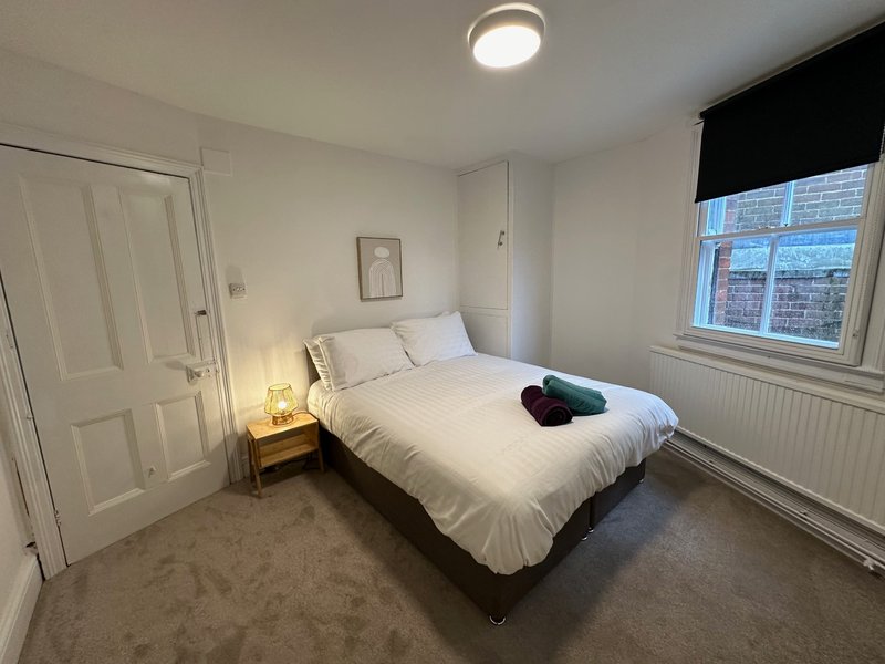 Bright bedroom with double bed, bedside lamp, wardrobe and window with black blind