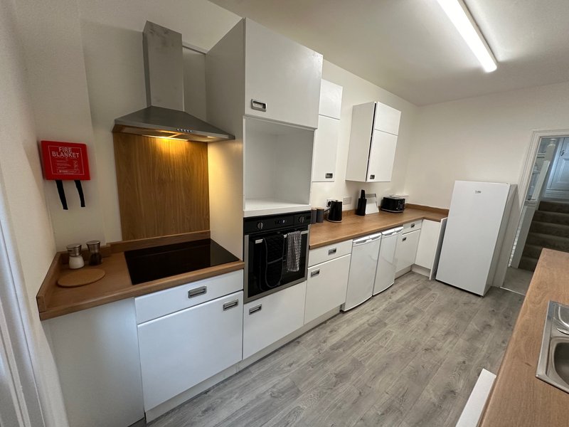Modern kitchen with white cabinetry, wooden countertop, integrated appliances and red fire alarm
