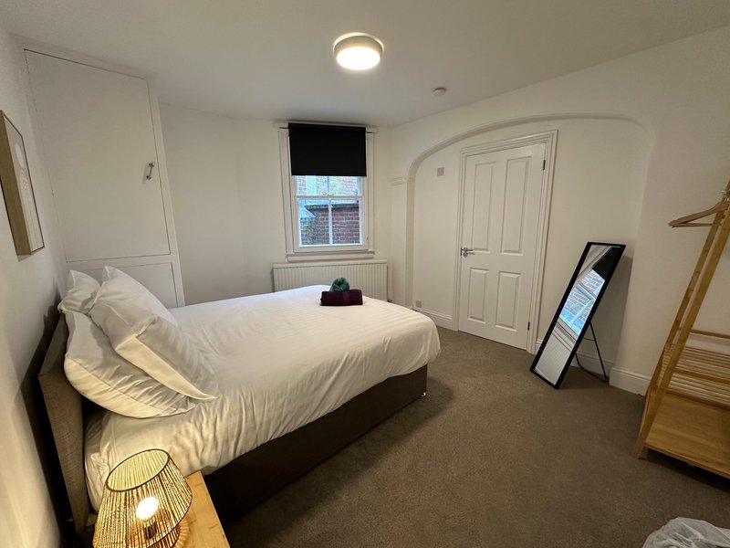Bright bedroom with double bed, white bedding, wooden wardrobe, and window with blind