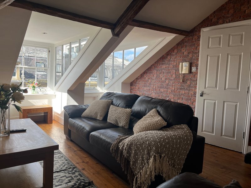 Bright loft-style living room with black leather sofa, exposed beams, brick wall and large skylight windows