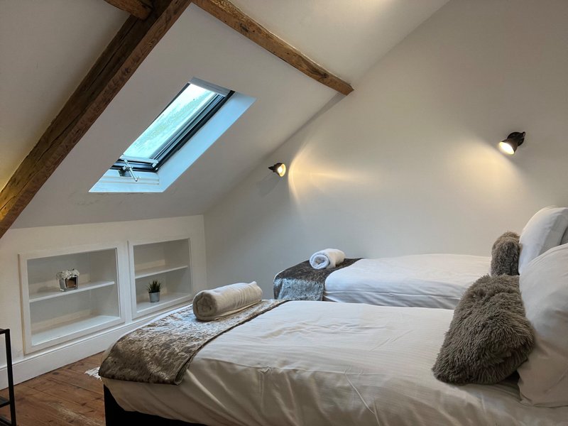 Bright attic bedroom with two beds, skylight window, wooden beams and storage shelving