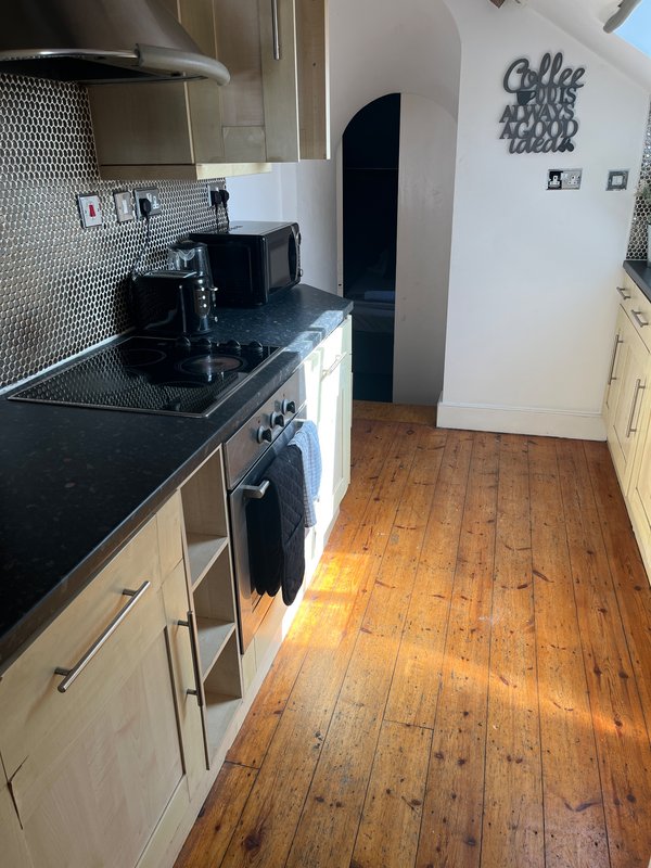 Modern kitchen with black countertop, white units, cooktop, and wooden flooring