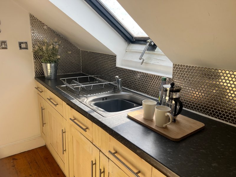 Compact kitchen with wooden cabinets, black countertop, stove, and skylight window