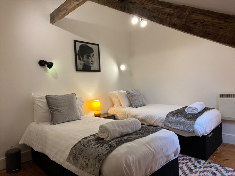 Twin bedroom with exposed beams, bedside lamps, cushions and framed wall art