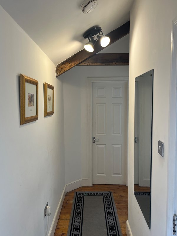 Hallway with wooden floor, white walls, framed artwork, and ceiling fan with light fixture