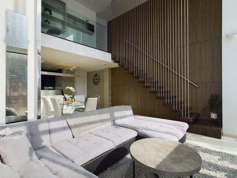 Modern open-plan living room with white sectional sofa, wooden staircase, and mezzanine level