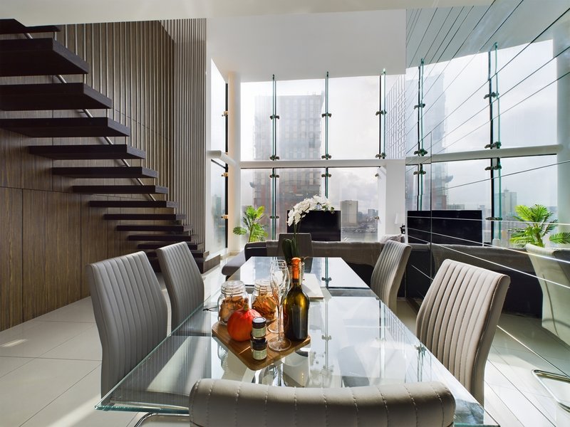 Modern dining room with glass table, striped chairs, floating staircase and floor-to-ceiling windows