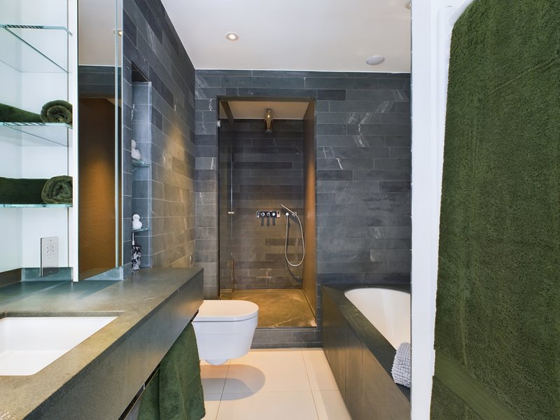 Modern bathroom with dark tile walls, double sink vanity, walk-in shower, and bathtub