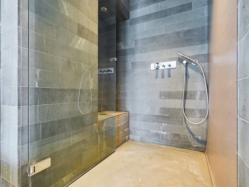 Modern bathroom with walk-in shower, grey tile walls, and wooden floor