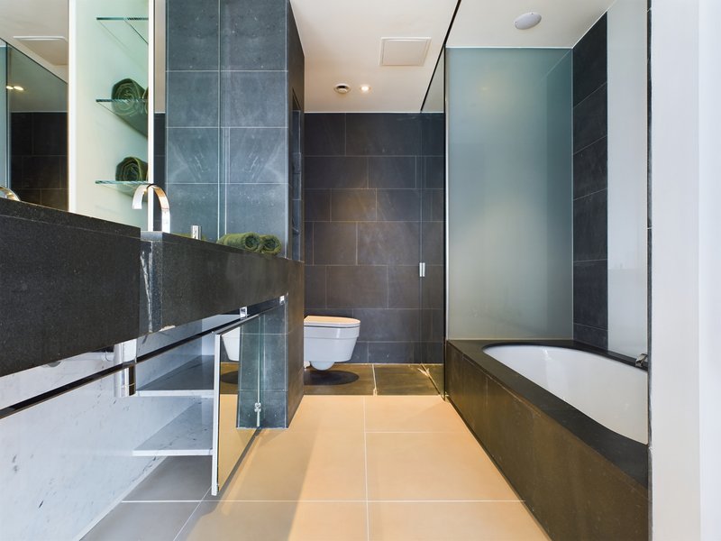 Modern bathroom with double vanity, dark tile walls, bathtub and toilet