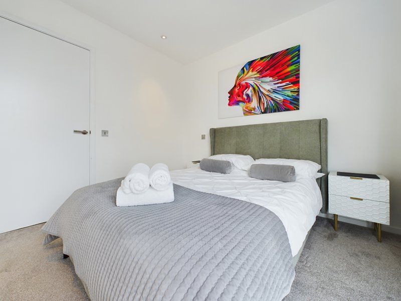 Modern bedroom with double bed, green headboard, white towels, colorful wall art