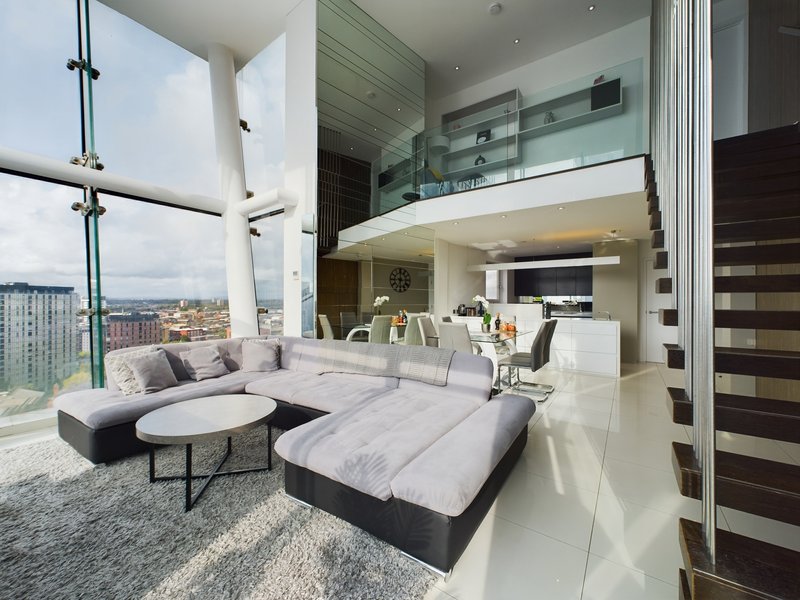 Modern open-plan living space with curved seating, marble table, kitchen area and city views