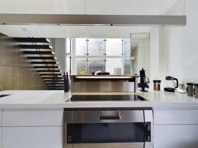 Modern kitchen with white counters, stainless steel appliances, and open staircase beyond
