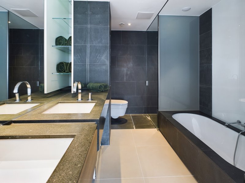 Modern bathroom with double vanity, dark tile walls, soaking tub and mirror