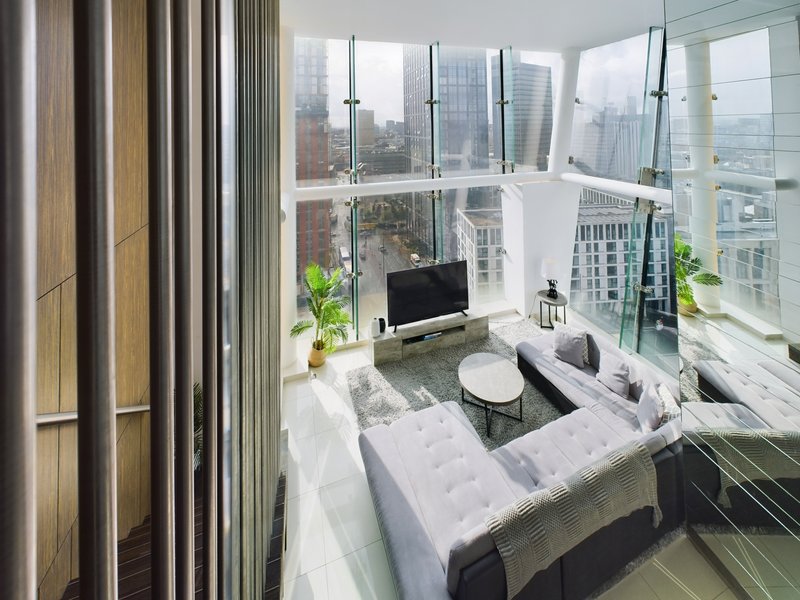 Modern studio apartment with floor-to-ceiling windows overlooking city skyline, white furnishings and plants