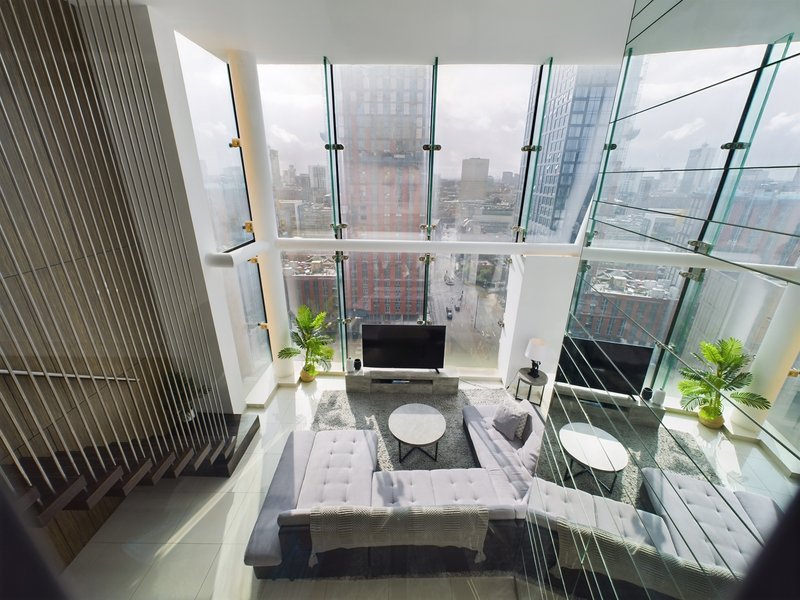 High-rise apartment interior with floor-to-ceiling windows overlooking city skyline, modern furniture and potted plants
