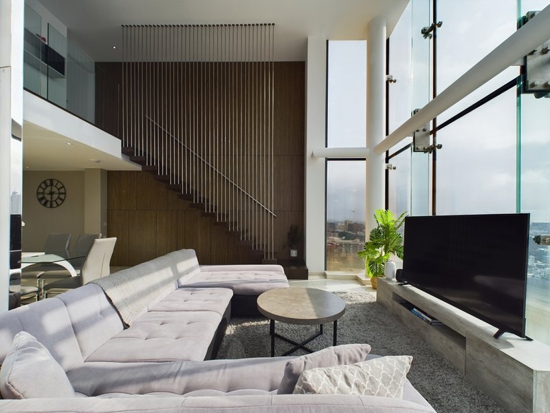 Modern open-plan living room with white sofa, TV, city views through floor-to-ceiling windows