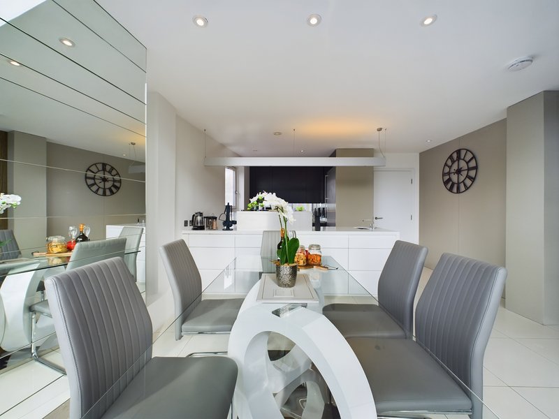 Modern open-plan kitchen and dining area with white cabinetry, dining table, grey chairs and clocks