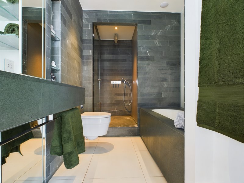 Modern bathroom with walk-in shower, toilet, vanity sink and green towels