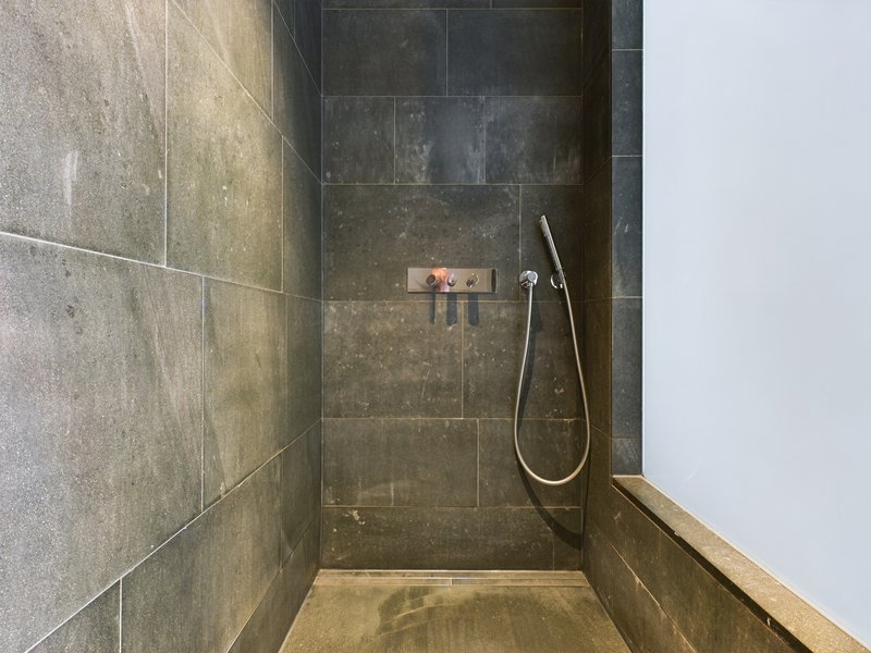 Modern bathroom shower enclosure with dark tile walls and handheld showerhead