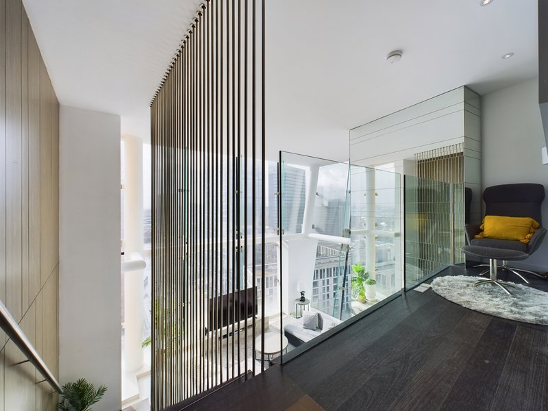 Modern hallway with dark flooring, vertical slat divider, glass partition, and yellow accent chair